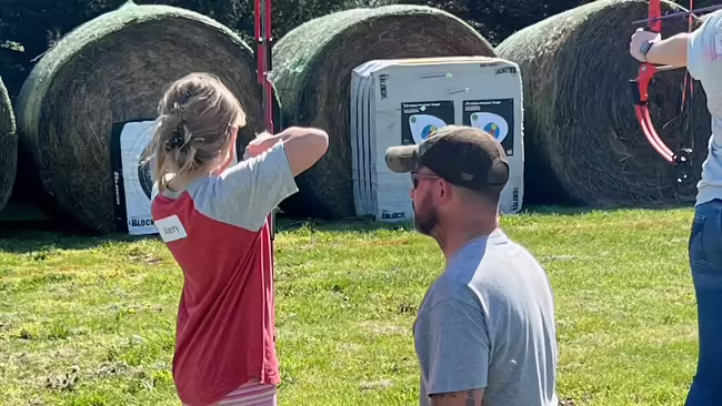 a girl shooting archery while an instructor looks on