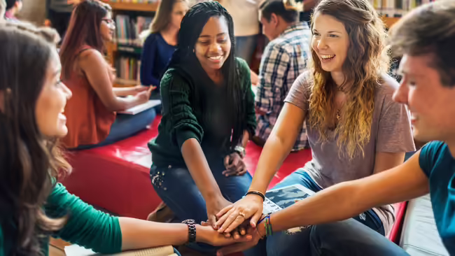 youth sitting with their arms outstretched and hands stacked in the middle of them