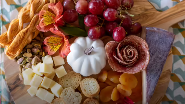 A charcuterie board featuring grapes, cheeses, crackers, dried apricots, pistachios, and salami.