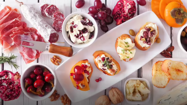 A platter of various appetizers including meats, cheeses, fruits, and bread.