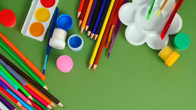 painting supplies and colored pencils on a green background