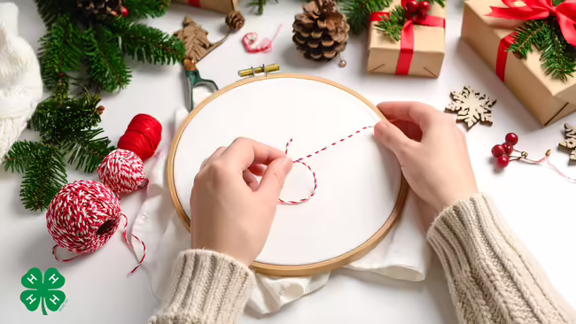 Hands preparing to embroider in a hoop, surrounded by holiday decorations and thread.