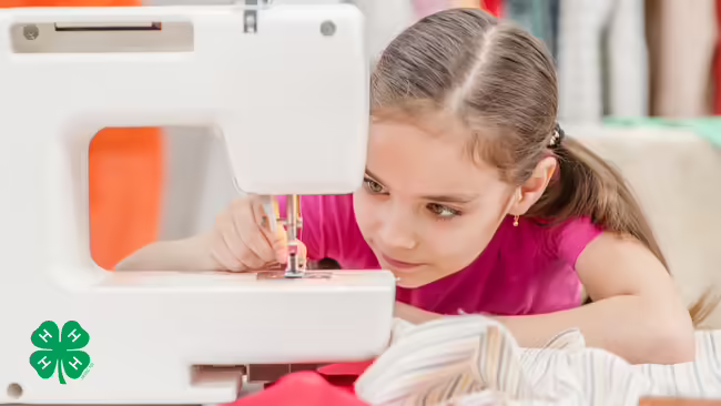 A girl focusing on the needle of a sewing machine. The green 4-H clover is in the bottom left corner.