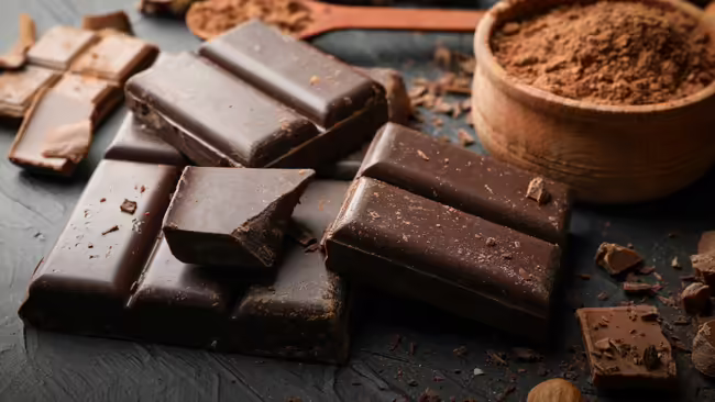 Chocolate bars, chunks and cocoa powder sitting on a gray table.