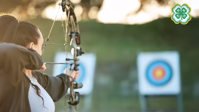A woman aims a bow and arrow at a target. A green 4-H logo is in the top right corner.