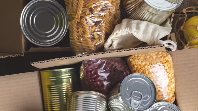A box filled with non-perishable food items, including canned goods, dry pasta, beans, and lentils, ready for donation in a food drive.