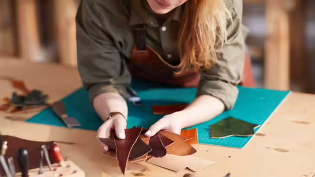 young lady holding leather scraps with leather tools nearby
