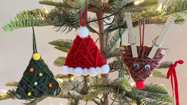 Christmas tree with three homemade yarn ornaments: a green triangular tree, a red Santa hat, and a brown reindeer face.