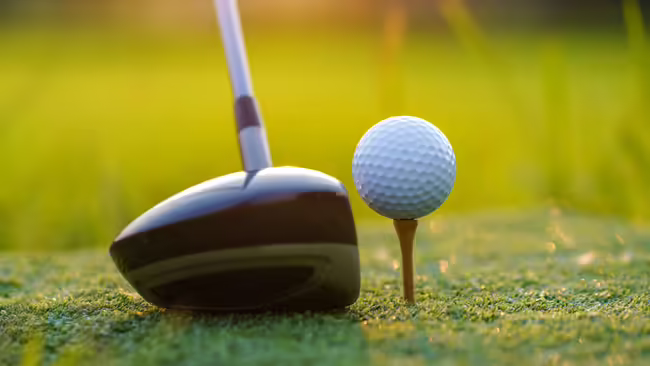 Golf ball sitting on a golf tee with a driver sitting next to it.