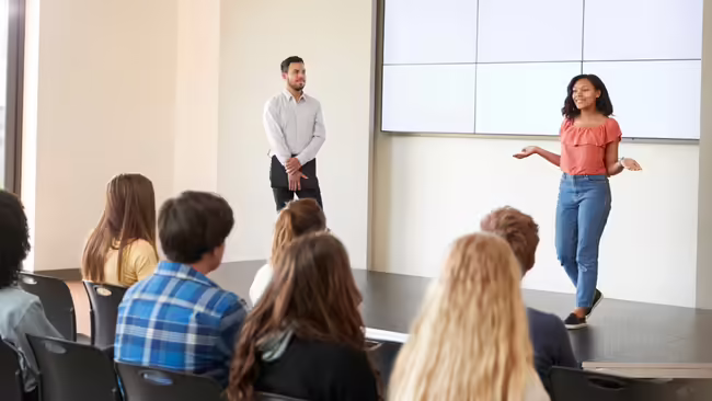 young girl speaking on a stage with a man nearby and people in the audience
