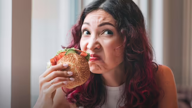 Woman with a disgusted expression eating a large sandwich.