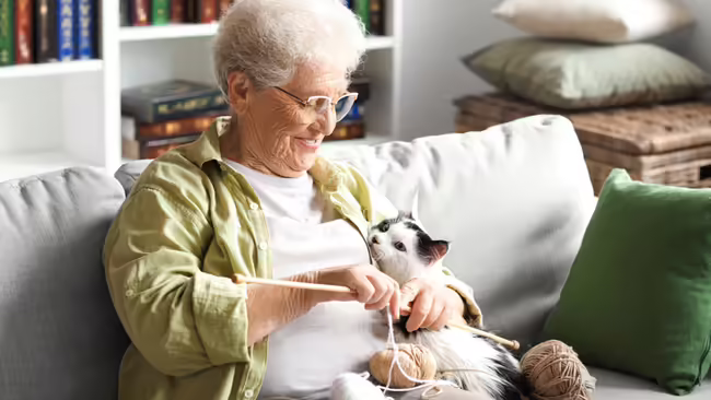older woman knitting with cat in arms