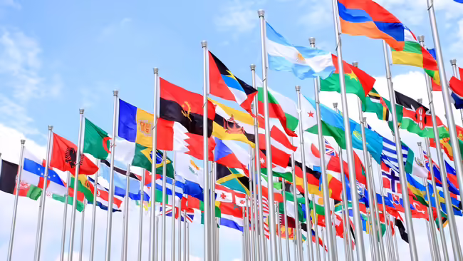 International flags on flag poles and light blue sky with clouds background