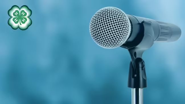 A microphone with a blue background. A green 4-H clover in the upper left corner.