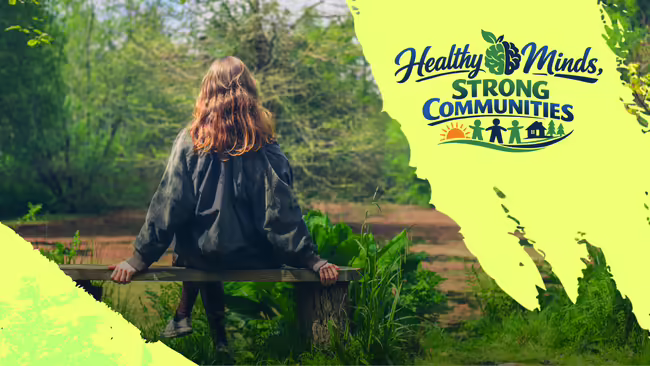 Woman sitting on a bench outside with the word "Healthy Minds, Strong Communities"