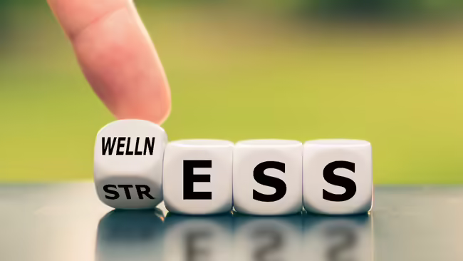 a finger moving a block that says "welln" and "str," next to blocks with letters "e, s, s" to spell wellness and stress 