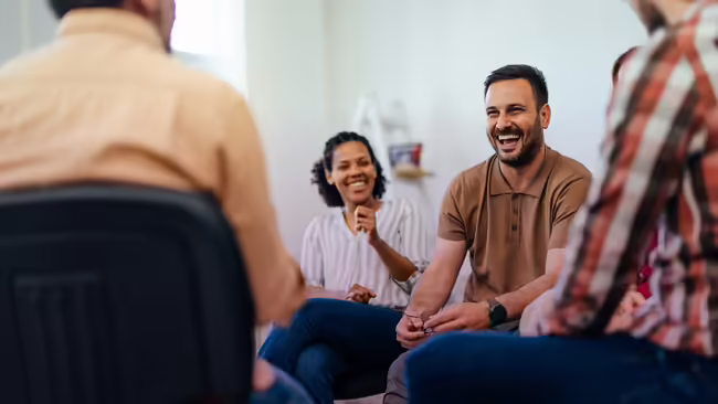   An adult man, looking happy, talking with people from the group therapy.