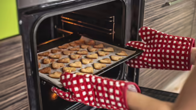 A pan of heart a shaped sugar cookies being removed from a black oven.