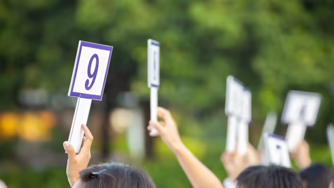 People holding signs with different numbers like at an auction.