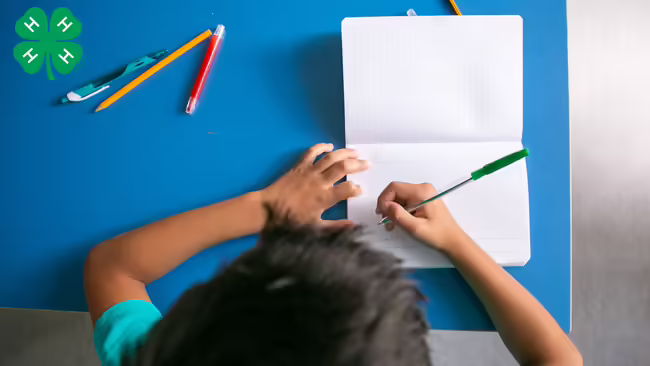 Youth writing on a notebook pad with a green clover on the left
