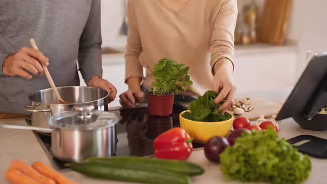 A couple cooking food in stainless steels saucepans.