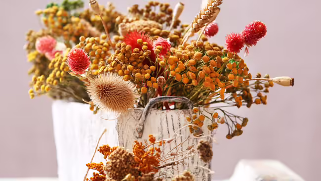 A fall flower arrangment in a white vase.
