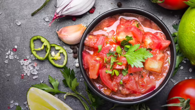 A bowl of salsa with salsa ingredients laid out around the bowl.