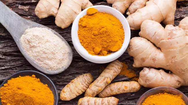 Ginger and turmeric ground and in spoons with fresh ginger nearby.