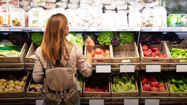 A woman shopping for fresh produce in the vegetable aisle of a grocery store.