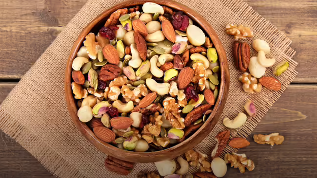A wooden bowl filled with a variety of mixed nuts and seeds.