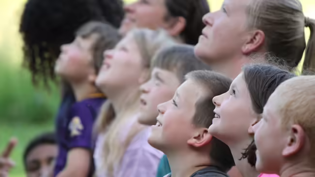Group of youth and an adult look to the sky with wonder.