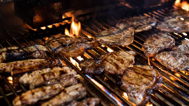 Pork chops are sizzling on a charcoal grill.