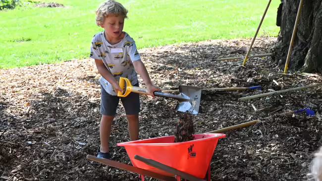 a little boy shoveling soil into a wheel barrel