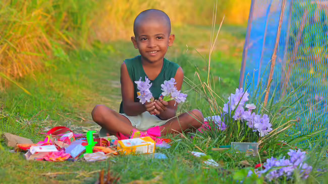 boy sitting on grass with purple flower