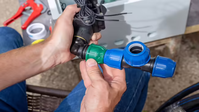 A man assembles a drip irrigation system by connecting pipeline elements and an automatic valve