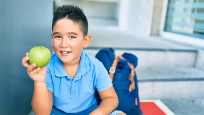 A boy in a blue shirt holds a green apple. 