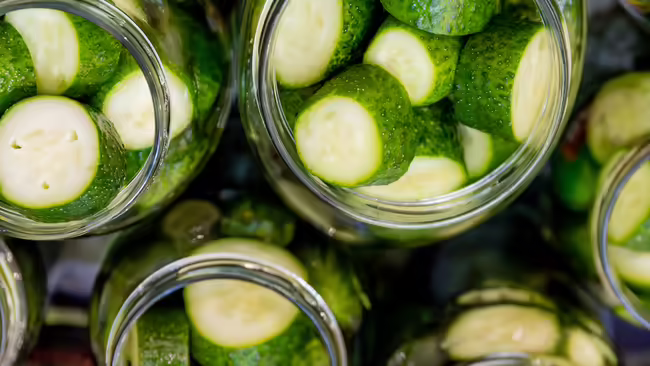 Sliced cucumbers packed into glass jars for pickling.