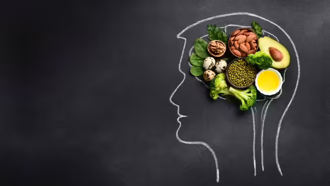 Chalkboard background with white chalk outline of male head. Brain-healthy foods on top of the board in the shape of a brain