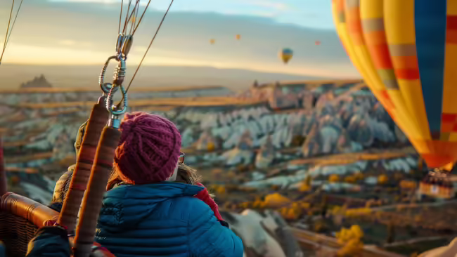 People in a hot air balloon gazing out at the horizon and other floating hot air balloons. 