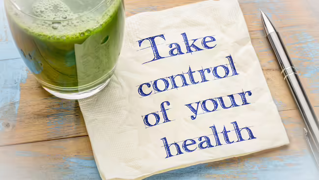 A napkin with the words, "Take control of your health" written on it, along with a class with a green smoothie in it.