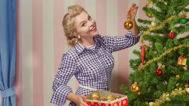 blonde woman putting ornament on tree smiling