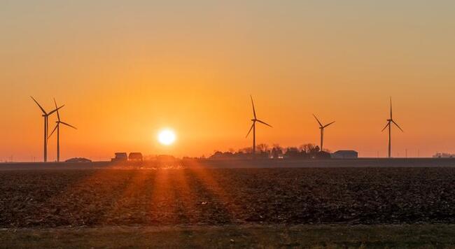 A sunrise over a farm field and wind turbines