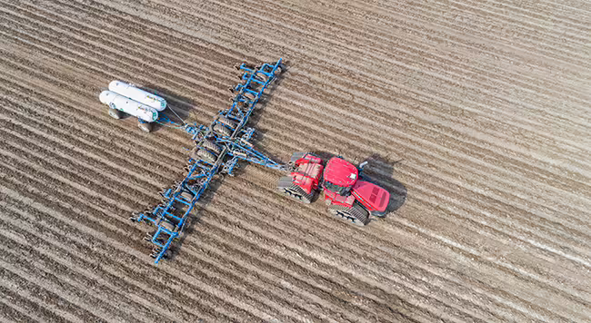 A tractor pulling anhydrous tanks across a field.