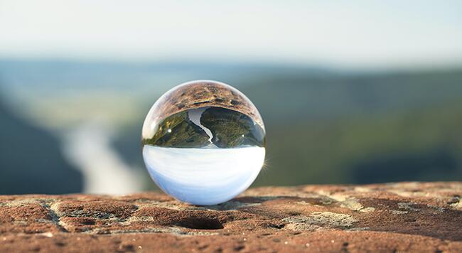 Clear photo globe sitting on rock edge reflecting earth, water, and nature scenes.
