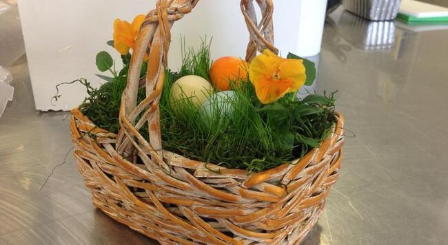 Wicker basket filled with live grass, flowers, and dyed eggs