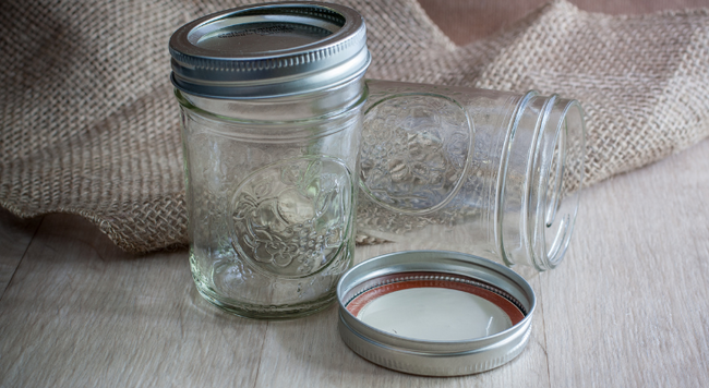 Two glass canning jars on a table, one standing up with the lid on, the other tipped sideways with the lid on the table