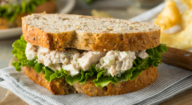Chicken salad sandwich with lettuce and bread, set on a napkin on top of a table. 