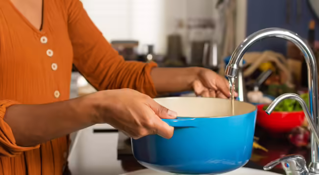 Women filling a blue pot with water at kitchen sink