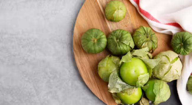 Tomatillos on a round wood board with a decorative red and white towel