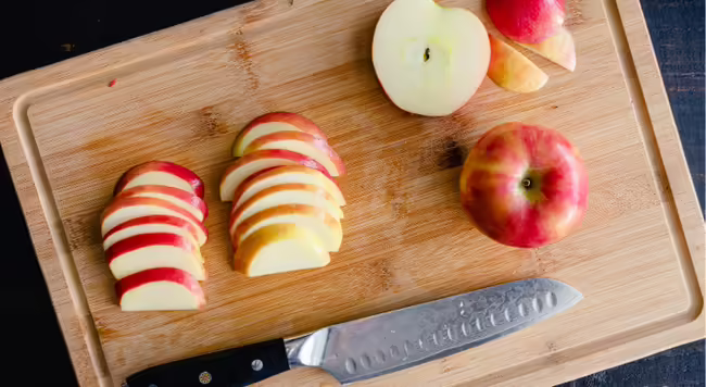 Sliced apples and apple halves on wood cutting board with knife